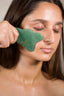 A woman using shanti3 green gua sha tool on her face.