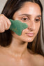 A woman using shanti3 green gua sha tool and freedom facial oil on her face.