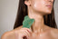 A woman using shanti3 green gua sha tool and freedom facial oil on her face.